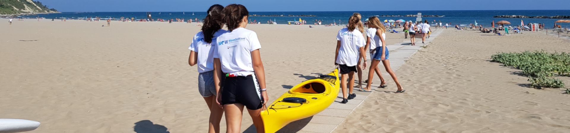 foto di ragazze sulla spiaggia di Pesaro che trasportano una canoa in acqua